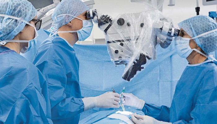 Three Neurosurgeons Seeing Microparts Of Patient Body Through Micro Lens In A Surgery Theatre.