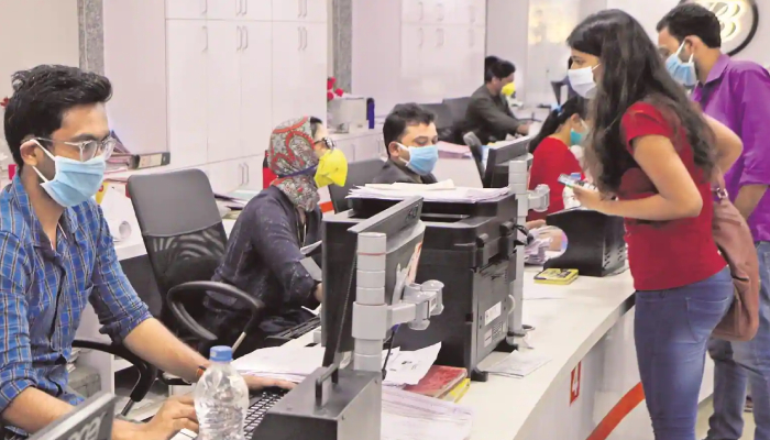 In a bank set up some customers are asking their queries with staff members who are seen with mask.
