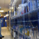 An employee in a warehouse checks stock in the shelves and makes notes in a notepad.